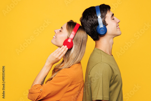 Quadro su tela Sideways young couple two friends family man woman wear shirt casual clothes together listen to music in headphones isolated on pastel plain light yellow background studio portrait
