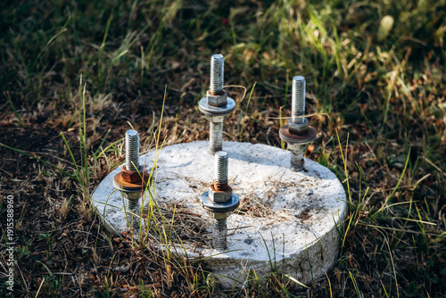 Fotografie Close-up of metal anchor bolts fixed in a circular concrete base embedded in gra
