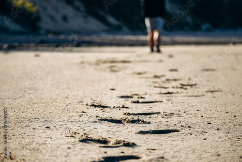 Wide sandy and rocky beaches at low tide along the St Lawrence River, with forested hills in the background and long human footprints leading across the empty shoreline in warm evening light