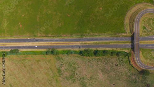 An aerial view of a winding road cutting through a lush green landscape with fields and trees