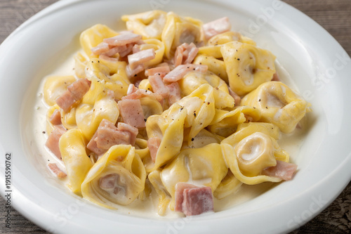 Obraz na plátně Close up of Italian tortellini pasta with cream sauce and cooked ham served in a white plate on a rustic table