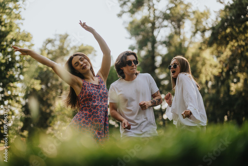 Bild auf Leinwand Three young adults dance in a sunny park, smiling and enjoying a carefree outdoor moment