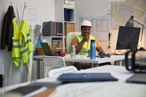 Fotografija Black middle aged male construction site foreman wearing hard hat working at des
