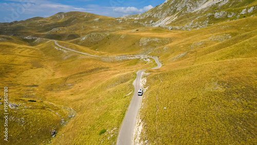 Aerial view of a camper van driving along a winding road at Sedlo Pass in Durmitor, Montenegro, surrounded by rugged mountain landscapes, capturing freedom, adventure, and scenic road travel.