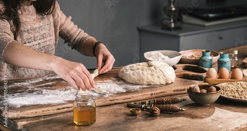 In a cozy kitchen, a person carefully shapes dough on a wooden table, surrounded by flour, eggs, and jars of honey, creating a special bread from scratch