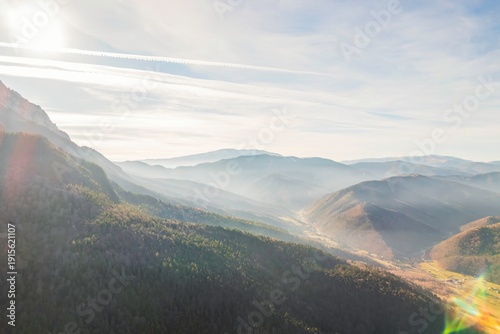 Golden sunlight spills over majestic mountains, illuminating a peaceful valley. Gentle mist weaves through the hills, creating a serene and dreamy atmosphere as the day begins
