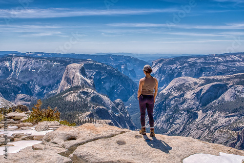 A woman stands on a mountain top, looking out over the landscape