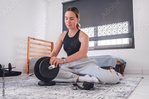 Fotografie Home workout, young woman setting up barbell for strength training, indoor home gym routine, fitness equipment and wellness lifestyle