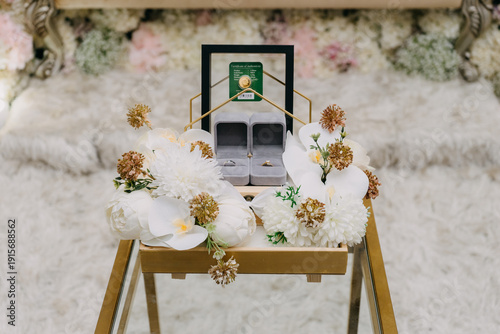 Canvastavla A close-up of a decorative wooden tray featuring a pair of wedding rings in velvet boxes, a certified gold dinar coin, and white orchid floral arrangements