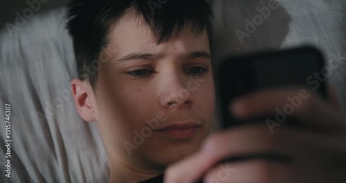 Teenage boy using a smartphone while lying in bed at night.