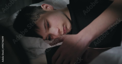 Teenage boy scrolling on a smartphone in bed at night