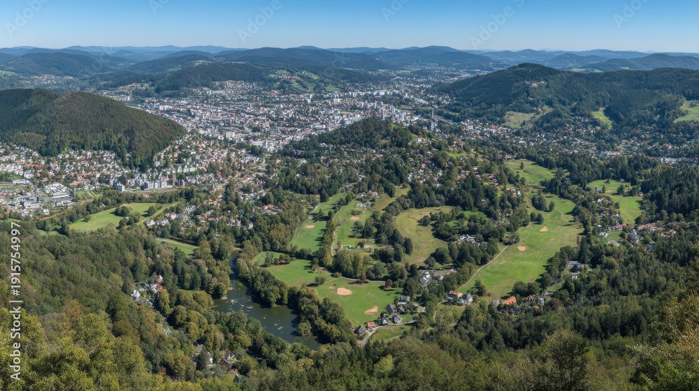 Fototapeta premium Panoramic View of Lush Green Landscape Overlooking a Scenic Town Surrounded by Rolling Hills and Clear Blue Sky on a Sunny Day