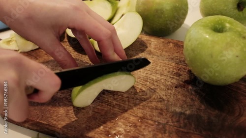 Close-up of a person slicing fresh, juicy green apples on a wooden cutting board in a bright kitchen, preparing healthy organic fruit snacks. Aesthetic video of cooking at home. 