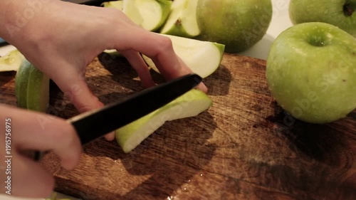 Close-up of a person slicing fresh, juicy green apples on a wooden cutting board in a bright kitchen, preparing healthy organic fruit snacks. Aesthetic video of cooking at home. 