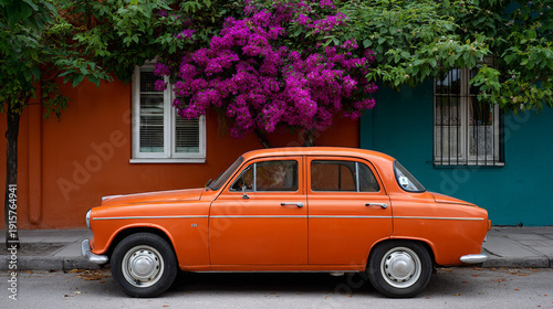 Vintage orange car parked by vibrant purple flowers and colorful wall  
