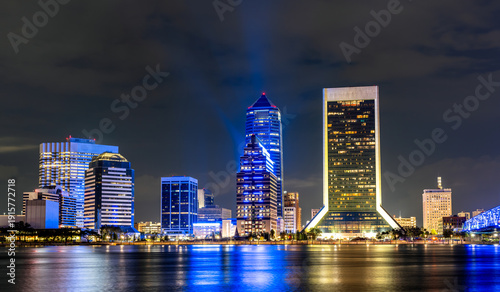 Jacksonville, Florida downtown skyline at night. Scenic view features illuminated skyscrapers including the Wells Fargo Center and Bank of America Tower reflecting in the St. Johns River