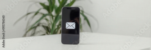 Smartphone displays email icon with green plant in background on a white table