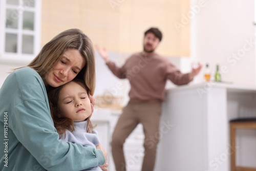 Alcohol addiction. Drunk man in kitchen, focus on his scared wife and daughter