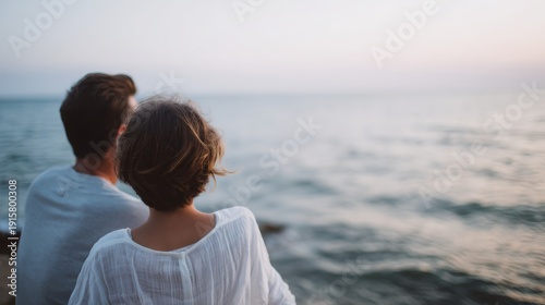 Man and a woman are sitting on a rock by the ocean