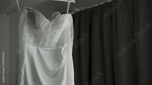 A white wedding dress hangs on a chandelier by the window