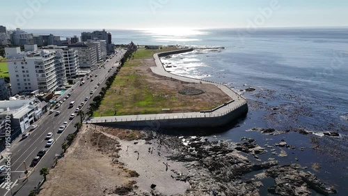 Drone orbits right at Mouille Point Beach to have a view of Signal Hill and other major landmarks on a sunny day in Green Point, Cape Town, South Africa