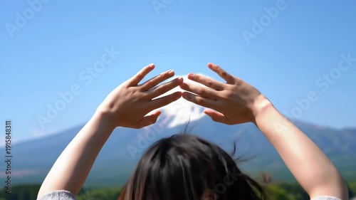 A womans hands frame the majestic Mount Fuji, capturing its beauty under a clear blue sky.