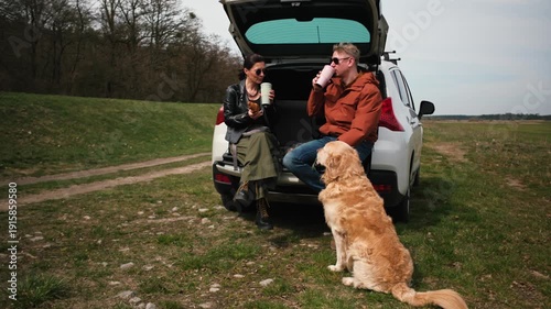 Wallpaper Mural Couple sits at the back of a car with a golden retriever dog on the grass. They chat and eat snacks in a natural setting during the daytime. Torontodigital.ca