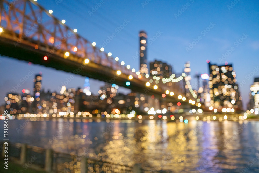 Fototapeta premium Soft colorful lights from the Queensboro Bridge and Manhattan skyline blur together in a dreamy bokeh scene. Reflections shimmer across the East River, creating an artistic and atmospheric city view.