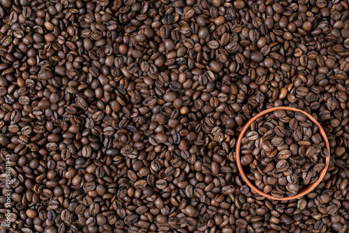 Top view of a small clay bowl filled with roasted coffee beans, placed on a background of scattered beans. Flat lay composition, selective focus. Concept of morning boost, specialty cafe, roastery