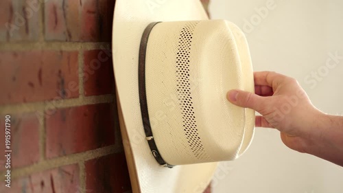 Person taking a straw cowboy hat off a hook