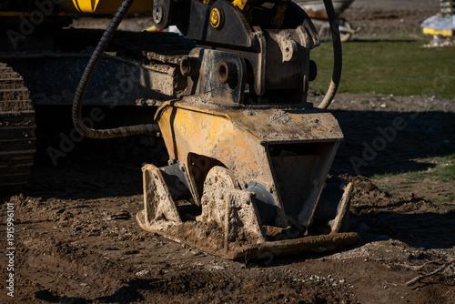 Closeup of excavator compactor attachment on fresh dirt on development construction job site
