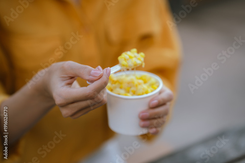 Foto Close-up of a woman in a yellow shirt eating melted cheese corn from a cup with a spoon, with soft bokeh lights in the background