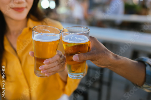 Two people clinking glasses of cold beer at an outdoor night market, celebrating with street food and evening lights in the background.