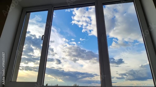 A multi-pane window reveals a vibrant blue sky filled with puffy, dramatic clouds