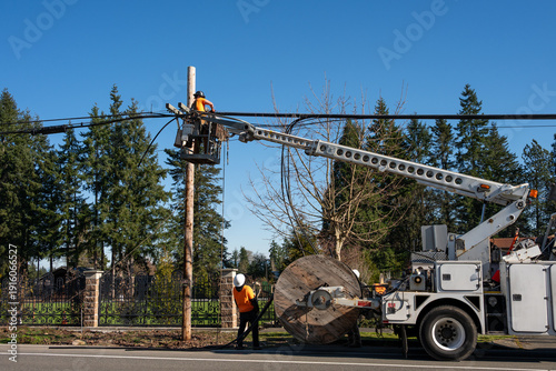 Power utility lineman in an aerial lift bucket upgrading utilities by replacing power lines and communication cable with fiber optics, work truck with cable spool
