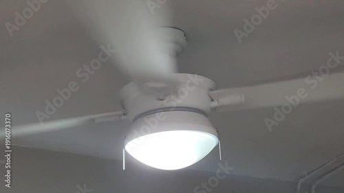 White ceiling fan spinning overhead mounted on the ceiling. The rapid rotation provides airflow and cooling for indoor comfort.
