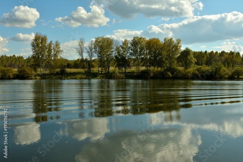 Ripples on the surface of a beautiful, wide lake surrounded by forest on a sunny summer evening.