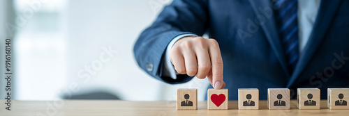 Close-up of businessman choosing a red heart block among people icons, representing workplace empathy, employee benefits, and human-centric corporate management