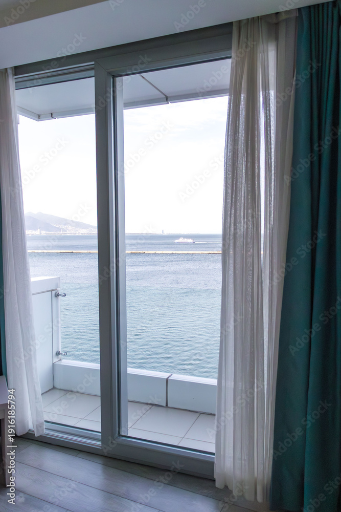 Fototapeta premium Cozy hotel room interior with sofa and table set with wine and fruit, overlooking marina and sea through large window.