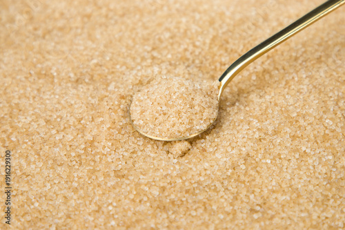 Φωτογραφία Brown sugar in a spoon on brown cane sugar background. Close up.
