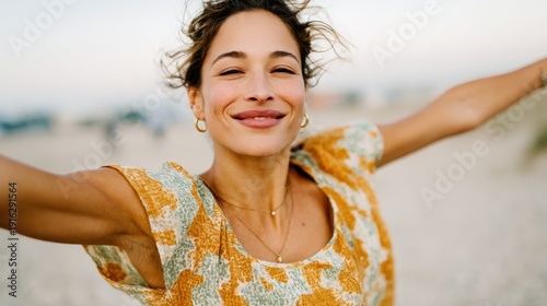 An exuberant woman with outstretched arms standing on the beach, embodying freedom and joy as she enjoys the feeling of the warm breeze and ocean waves around her.