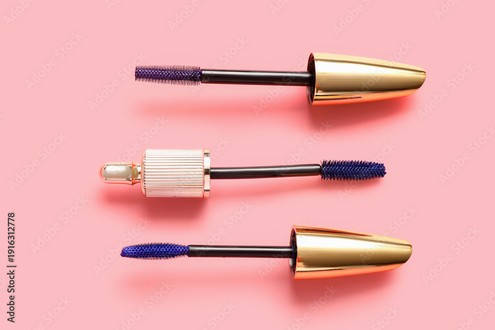 Fototapeta premium Different brushes of blue mascara on pink background, closeup