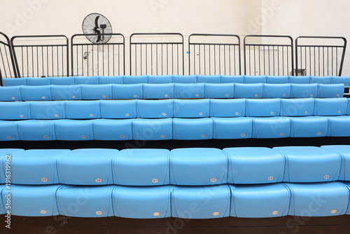 Fotografía Blue stadium seats in empty indoor arena with black safety railings and wall fan, sport bleachers background for events and spectators