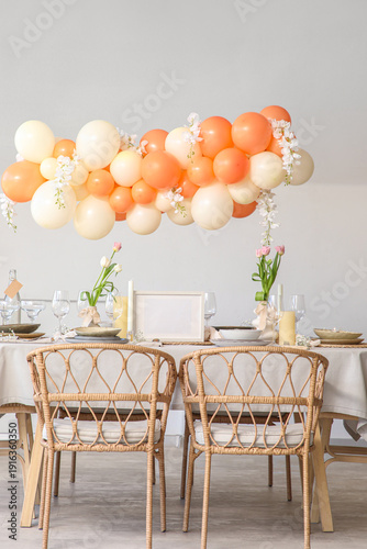 Elegant table setting with blank frame, beautiful flowers and balloons in light dining room