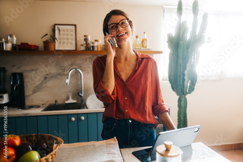 Woman on phone in cozy kitchen with laptop