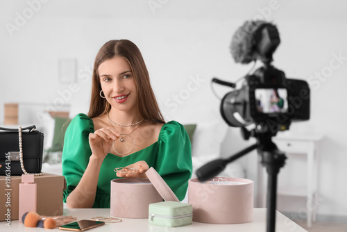 Happy young fashion blogger recording video on camera while unpacking new sty...