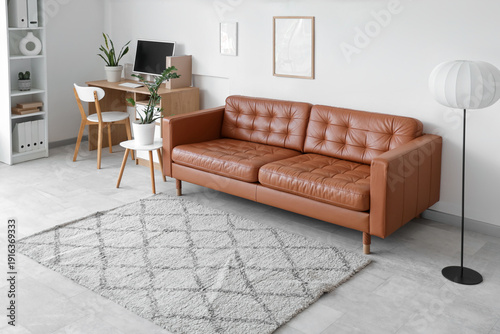 Interior of modern office with leather sofa, workplace and floor lamp near wh...