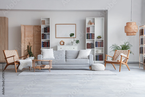 Bookcases, cozy sofa, wicker armchairs and coffee table in interior of stylish living room