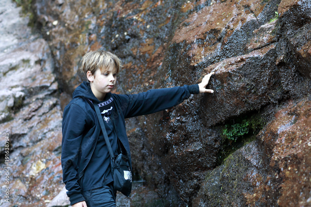 Obraz premium Boy touching wet rock at Cossack waterfall in Teberda Nature Reserve