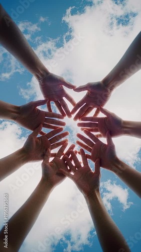 Circle of diverse human hands joining together against a blue sunny sky with clouds symbolizing unity and teamwork in a global community support or strong partnership concept